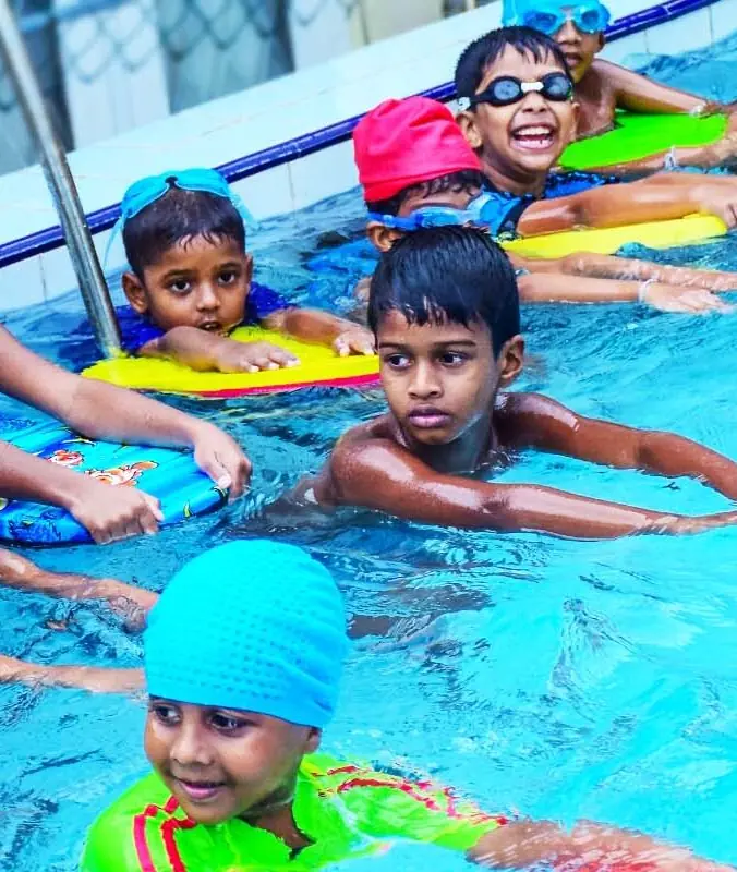 Children in swimming caps hold floats in a pool.