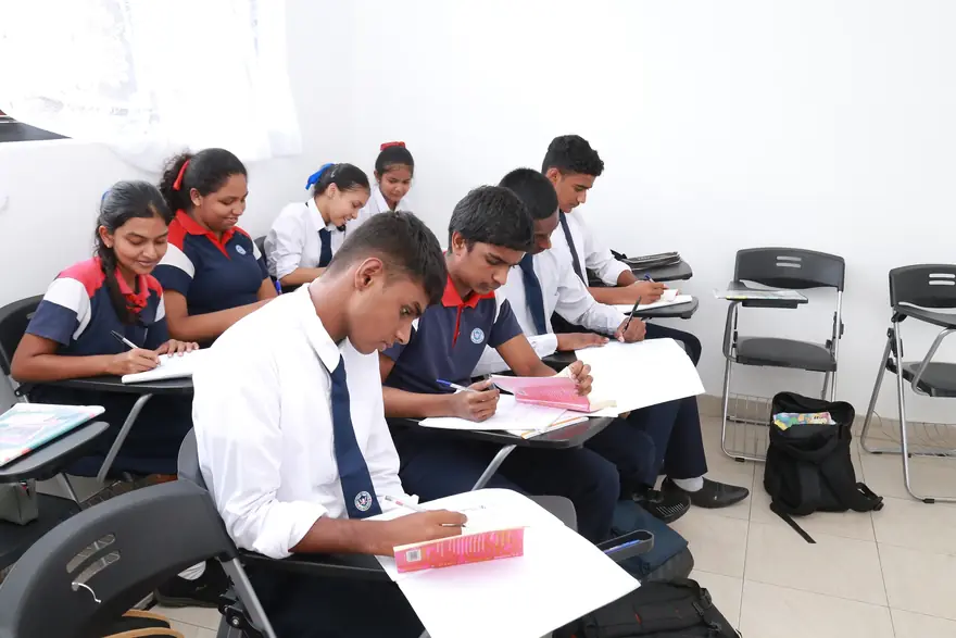 Pupils write in exercise books at their desks in a bright classroom.
